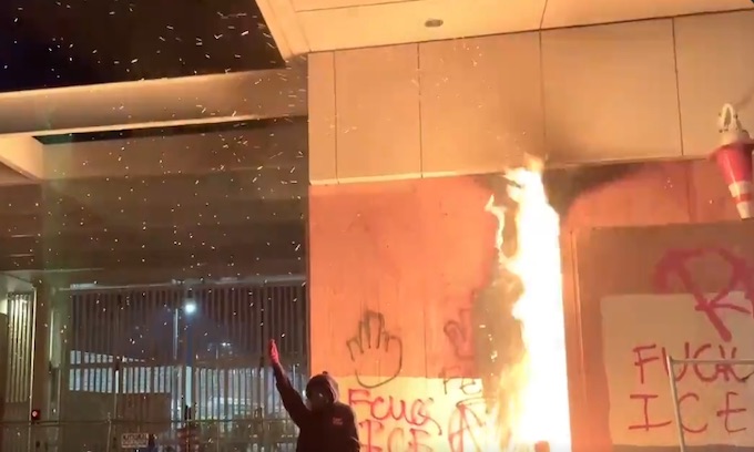 Antifa protesters in gas masks and waving black umbrellas torch ICE building in Portland